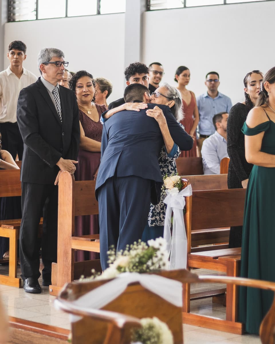 Dos personas se abrazan con emoción dentro de la iglesia, rodeadas de invitados