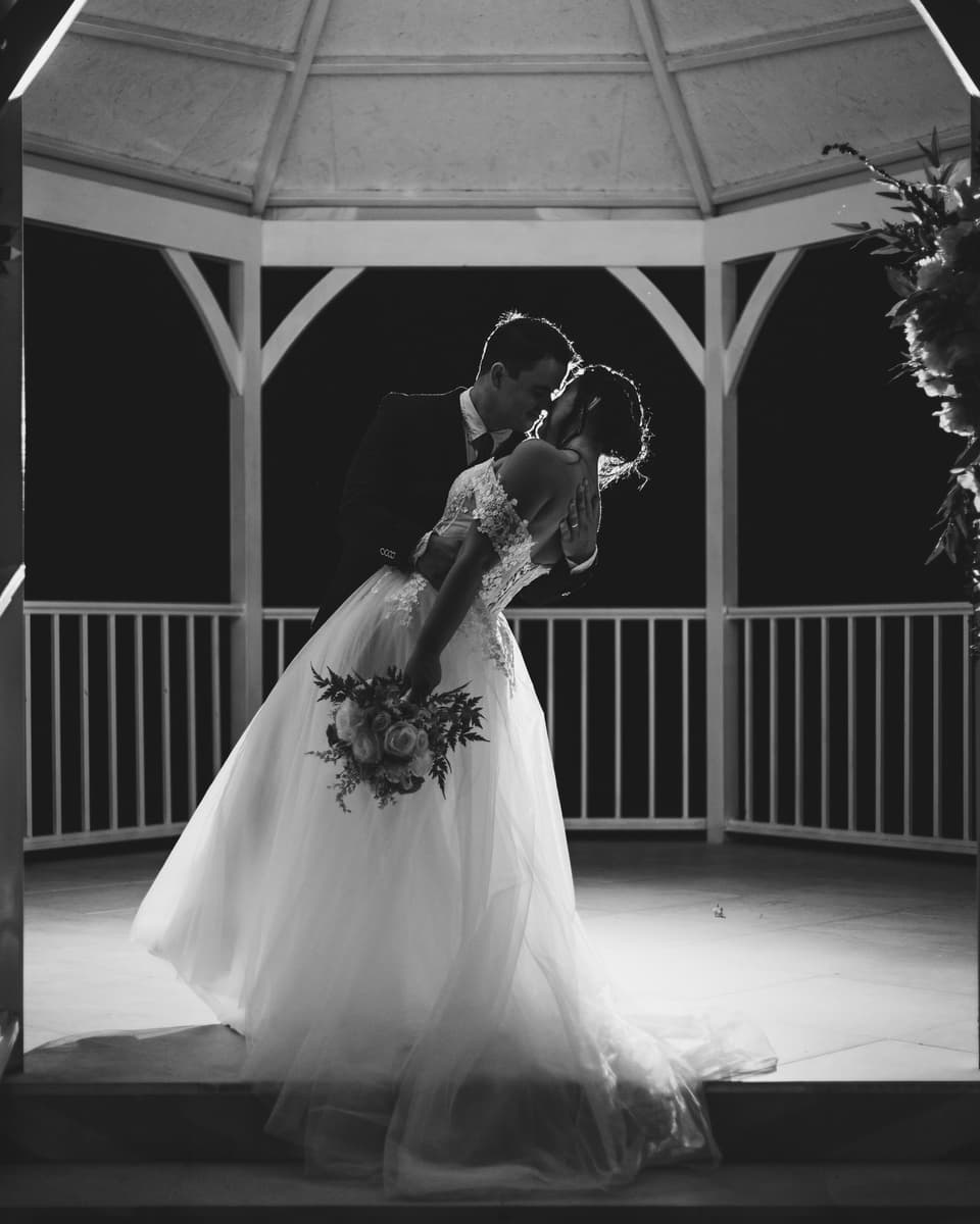 Beso inclinado de los novios dentro de un gazebo, en siluetas y blanco y negro