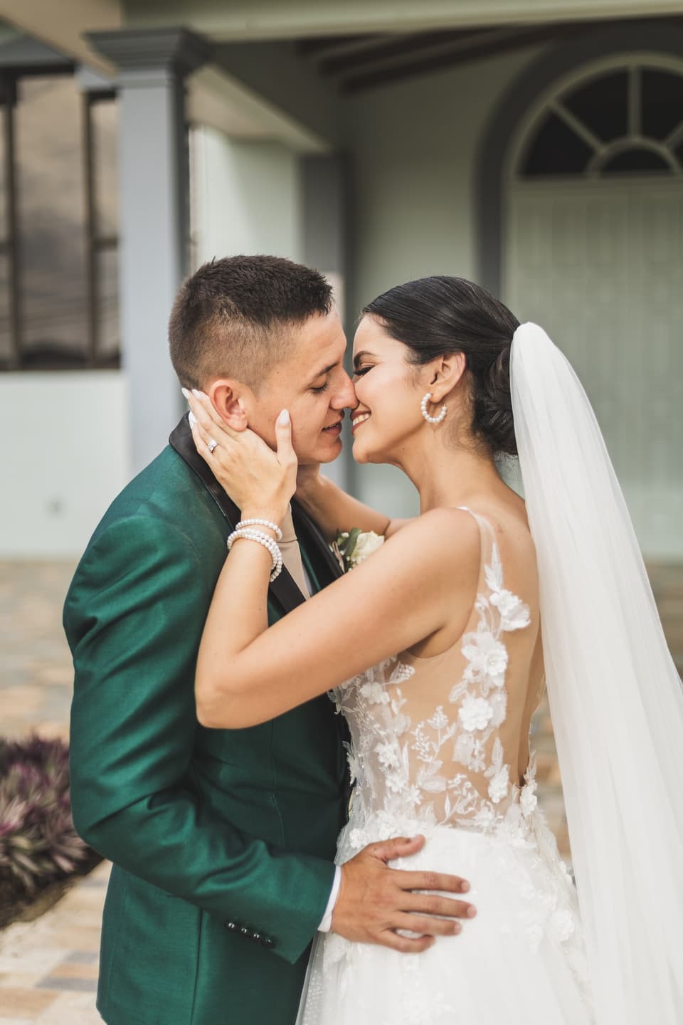 Novios besándose frente a una iglesia blanca, él con traje verde y ella con velo