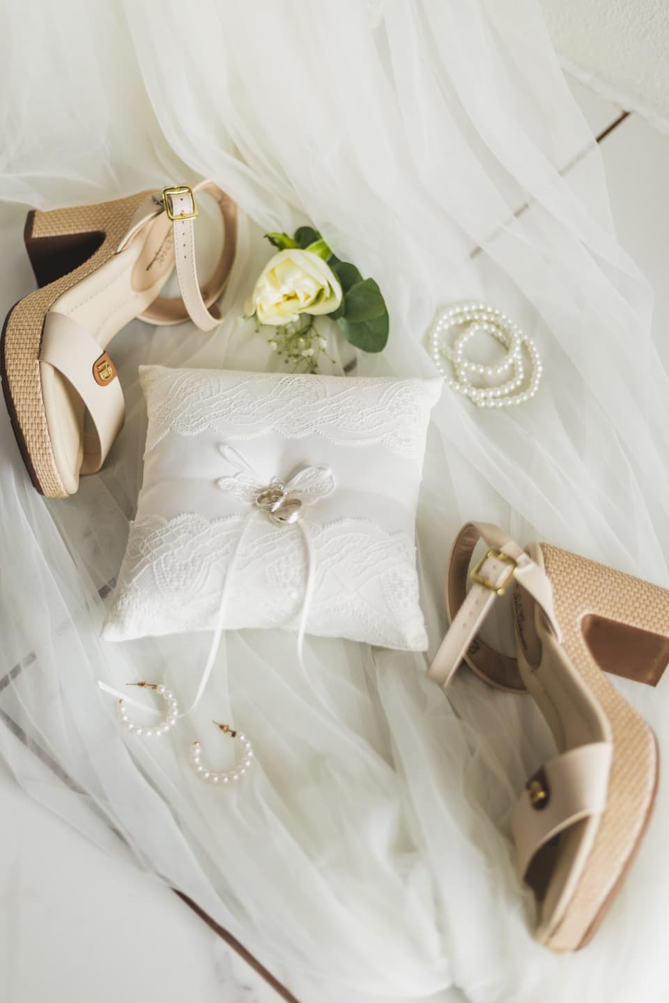 Zapatos de la novia, un cojín con los anillos, perlas y una flor sobre el velo