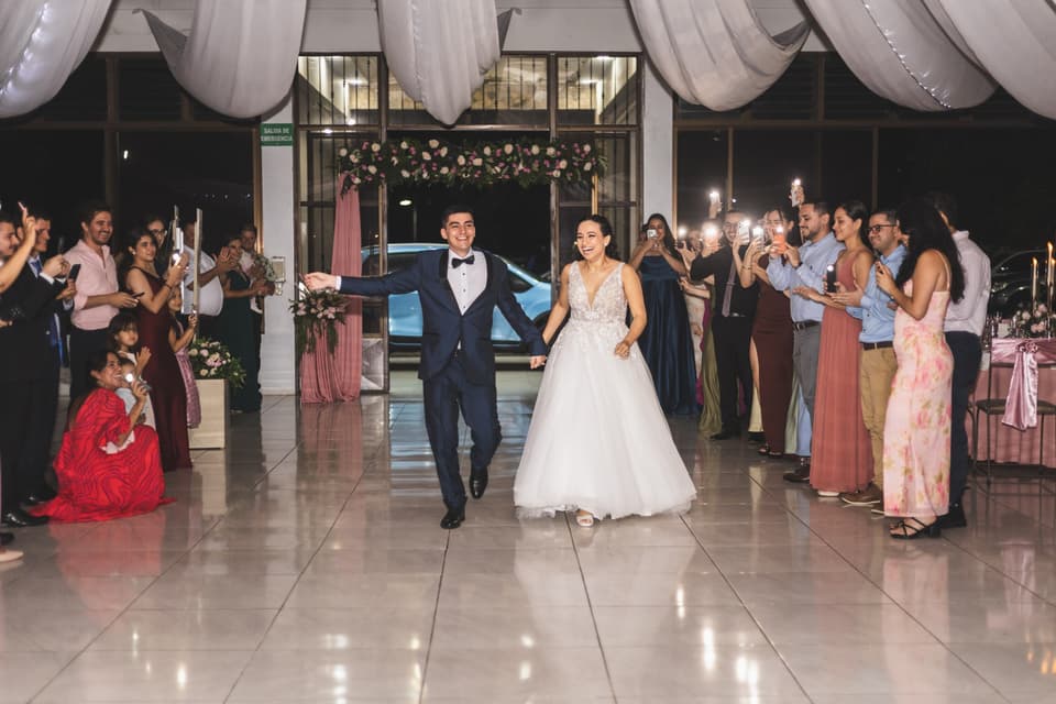 Novios entrando de la mano al salón de la recepción mientras los invitados los reciben