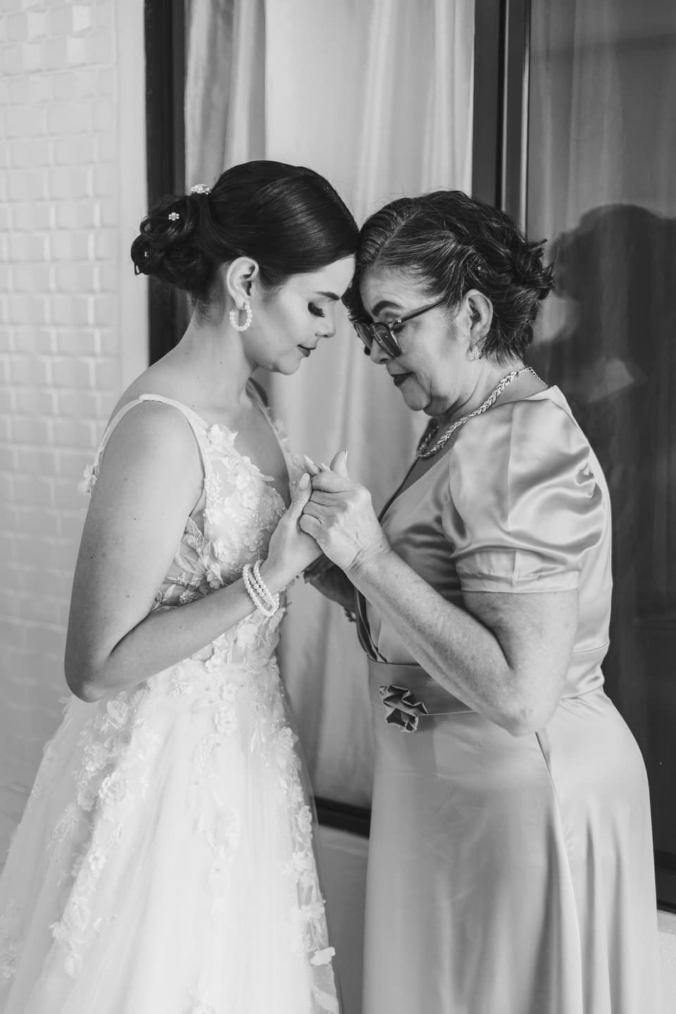 Novia y una mujer mayor tomadas de las manos, frente con frente, en blanco y negro