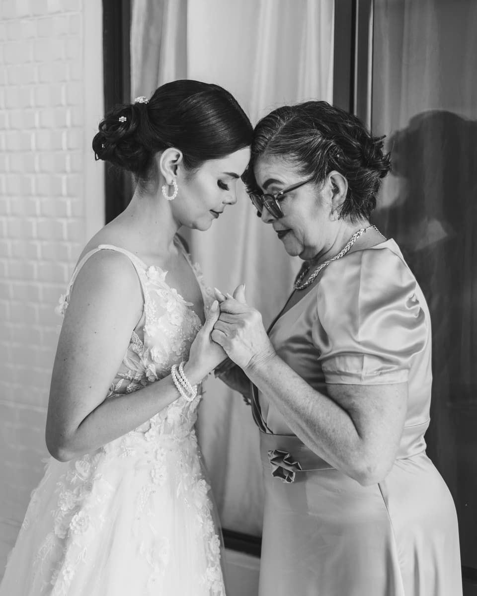 Novia y una mujer mayor tomadas de las manos, frente con frente, en blanco y negro