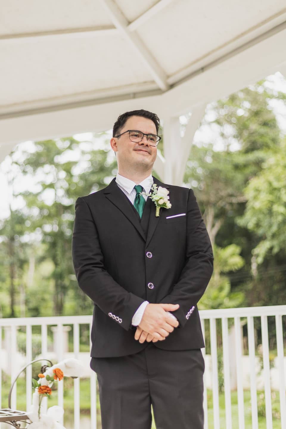 Novio esperando a la novia con una sonrisa y las manos juntas, bajo un toldo en el jardín