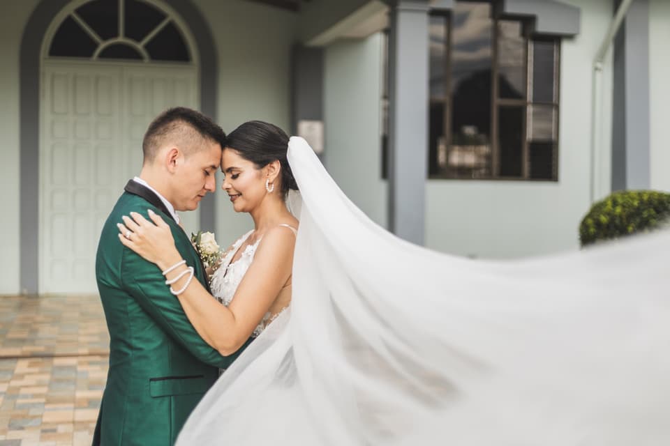 Novios abrazados frente a la iglesia mientras el viento levanta el velo