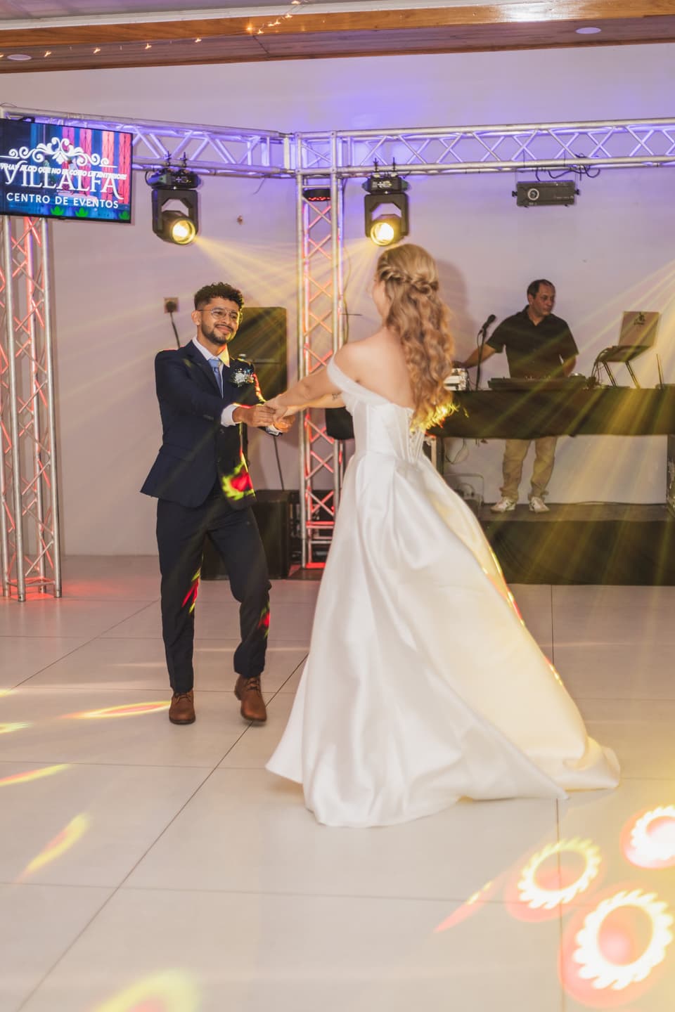 Novios en su primer baile sobre la pista, con luces de colores detrás