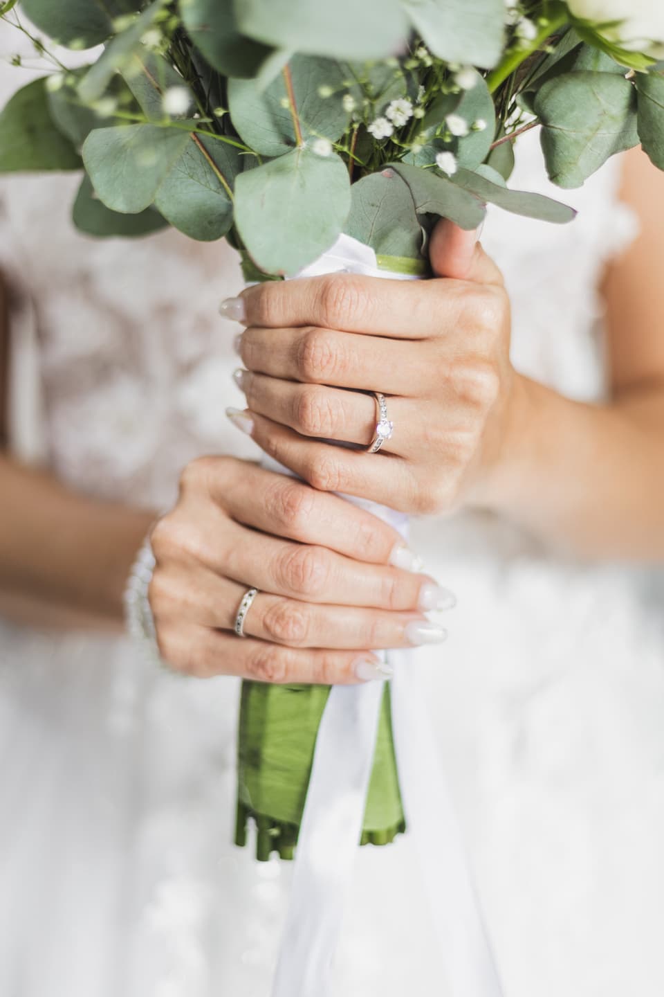 Manos de la novia con sus anillos sosteniendo un ramo de eucalipto y flores blancas