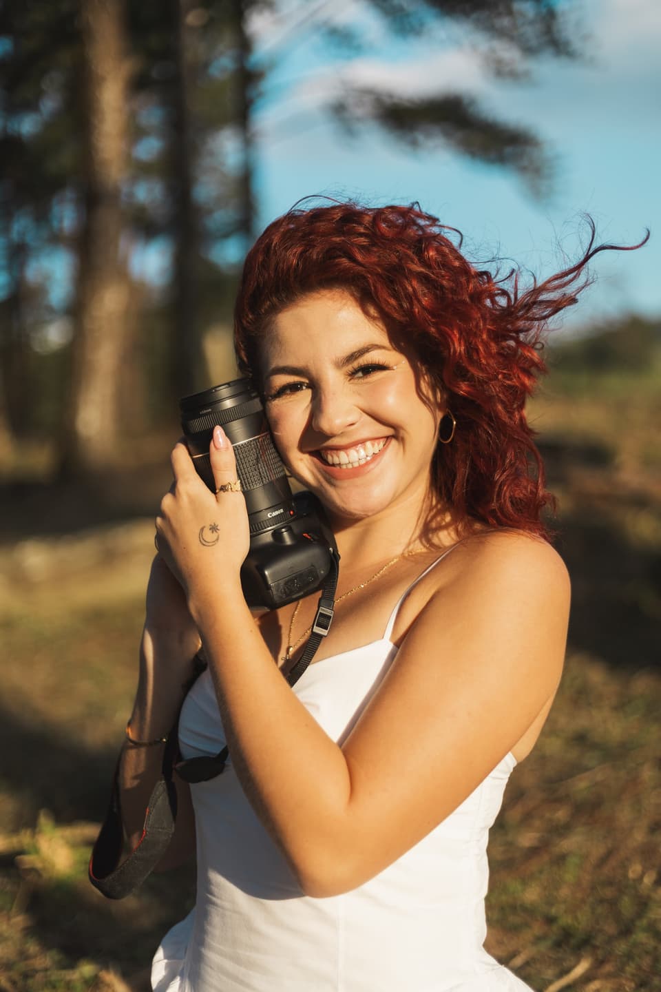 Fabiola Soto sonriendo con su cámara apoyada en el hombro, con el pelo al viento y luz de tarde